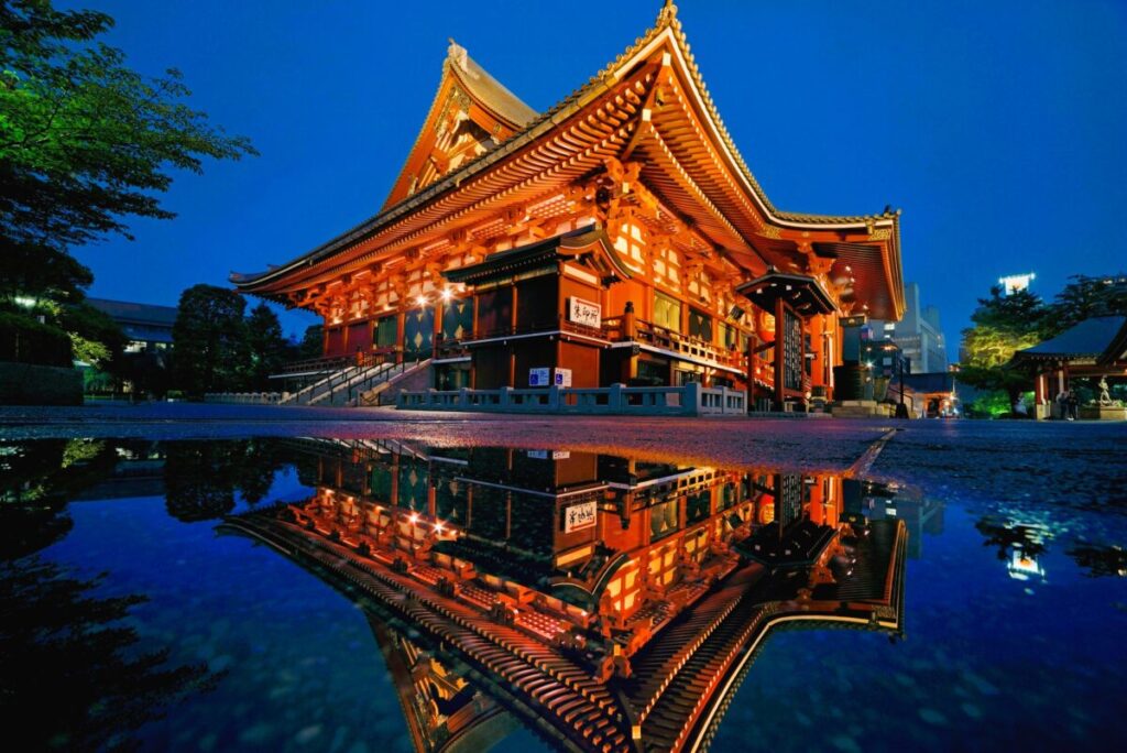 Illuminated main hall of Senso-ji Temple reflected in a puddle at night in Asakusa, Tokyo
